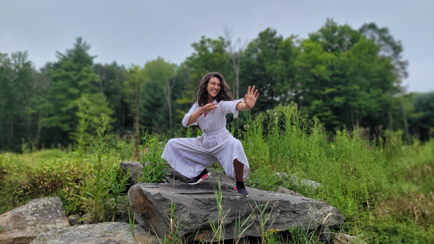 Brittany in a qigong stance on a rock in a green meadow