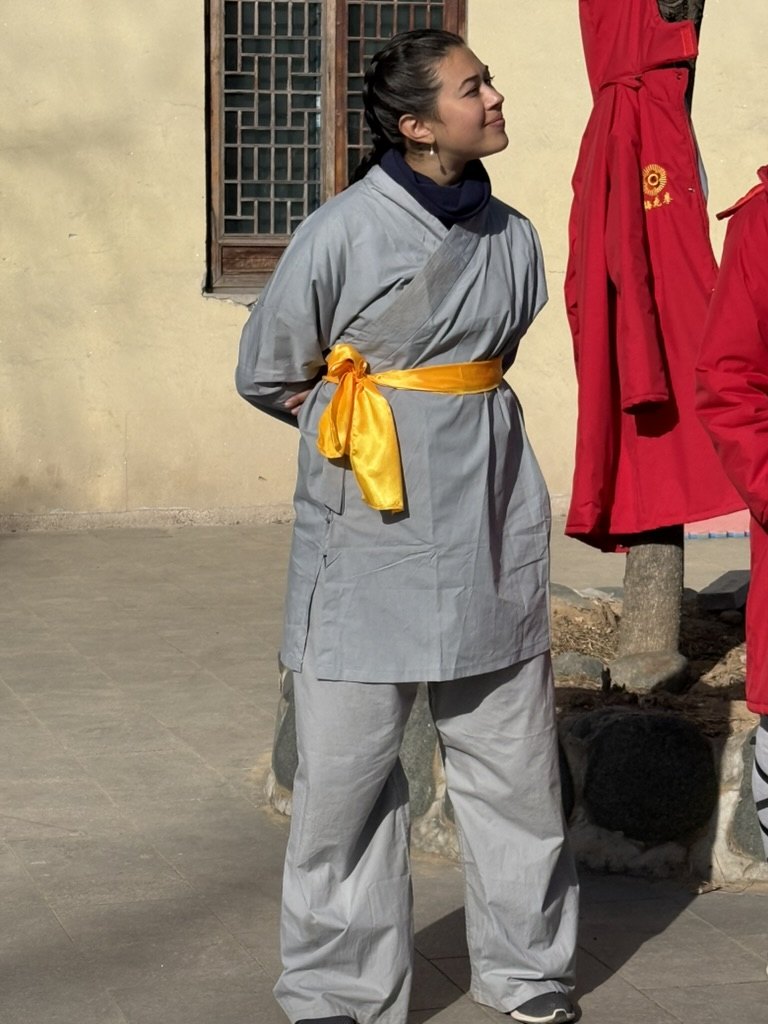 Brittany in traditional gray training clothes with a yellow sash in a temple courtyard